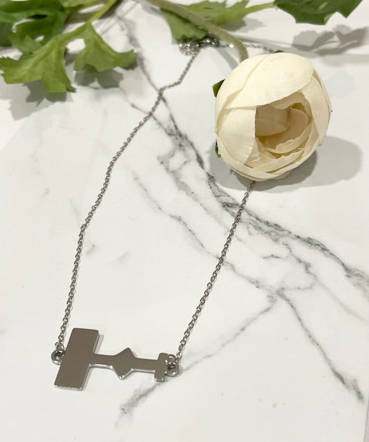 Eras Tour stage-shaped necklace with a polished silver finish displayed next to a white flower on a marble background.
