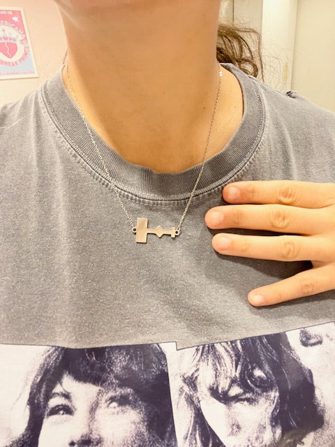 Close-up of a person wearing a silver necklace with a pendant shaped like the Taylor Swift Eras Tour stage layout.