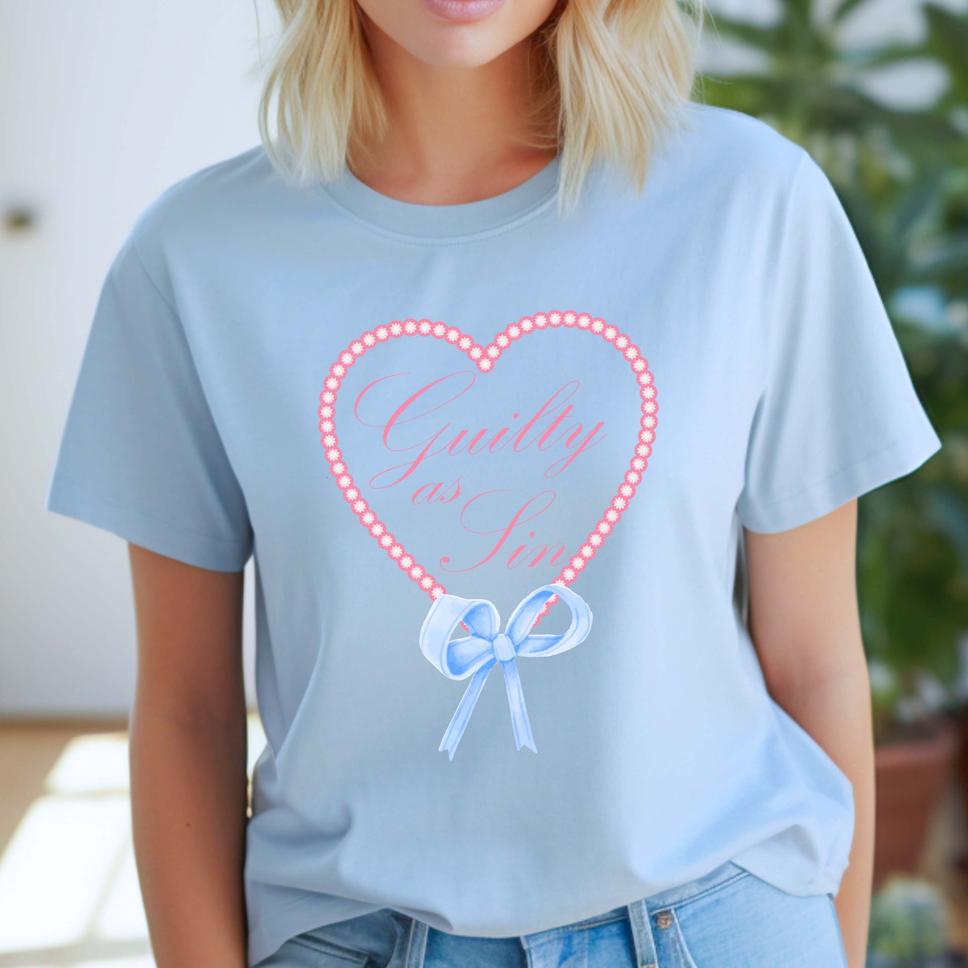 Taylor Swift-inspired baby blue t-shirt with the phrase “Guilty as Sin” in pink cursive inside a floral heart frame and finished with a soft blue bow design