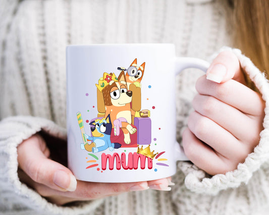 Woman holding a white ceramic mug with cartoon characters inspired by Bluey, featuring Mum, Bluey, and Bingo, with the word “mum” in colorful text below.