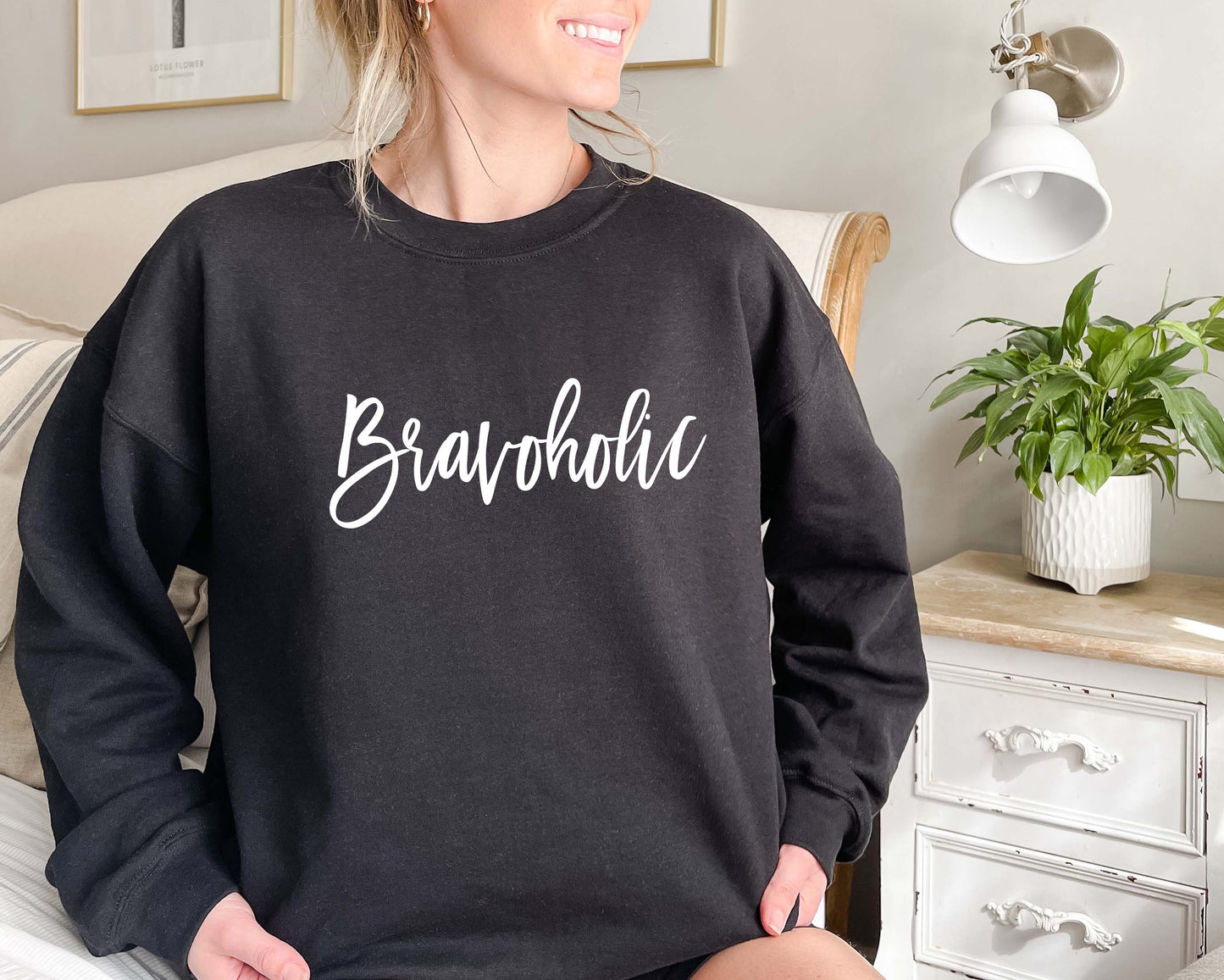 Woman lounging in a black Bravoholic crewneck sweatshirt on a cozy bed