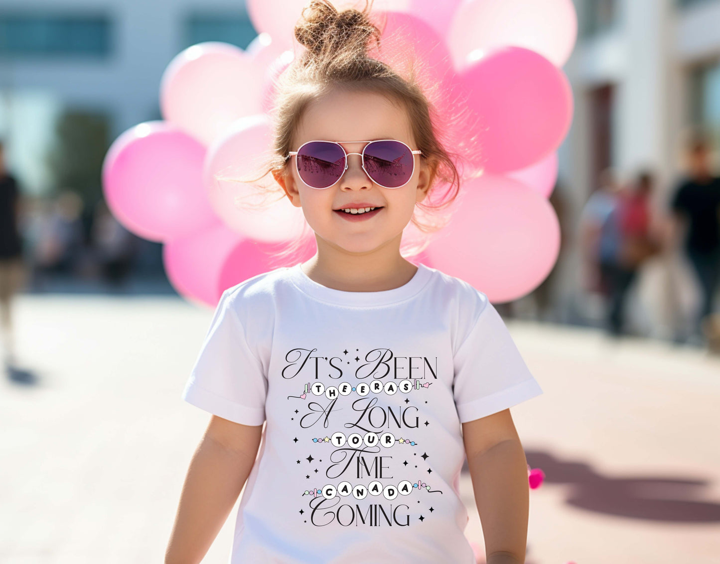 little girl wearing a white Taylor Swift-inspired t-shirt that reads “It’s Been a Long Time Coming” with The Eras Tour and Canada spelled out in friendship bracelet lettering