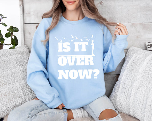 Woman wearing a light blue crewneck sweatshirt with the words “Is It Over Now?” in bold white text and bird silhouette graphic above.