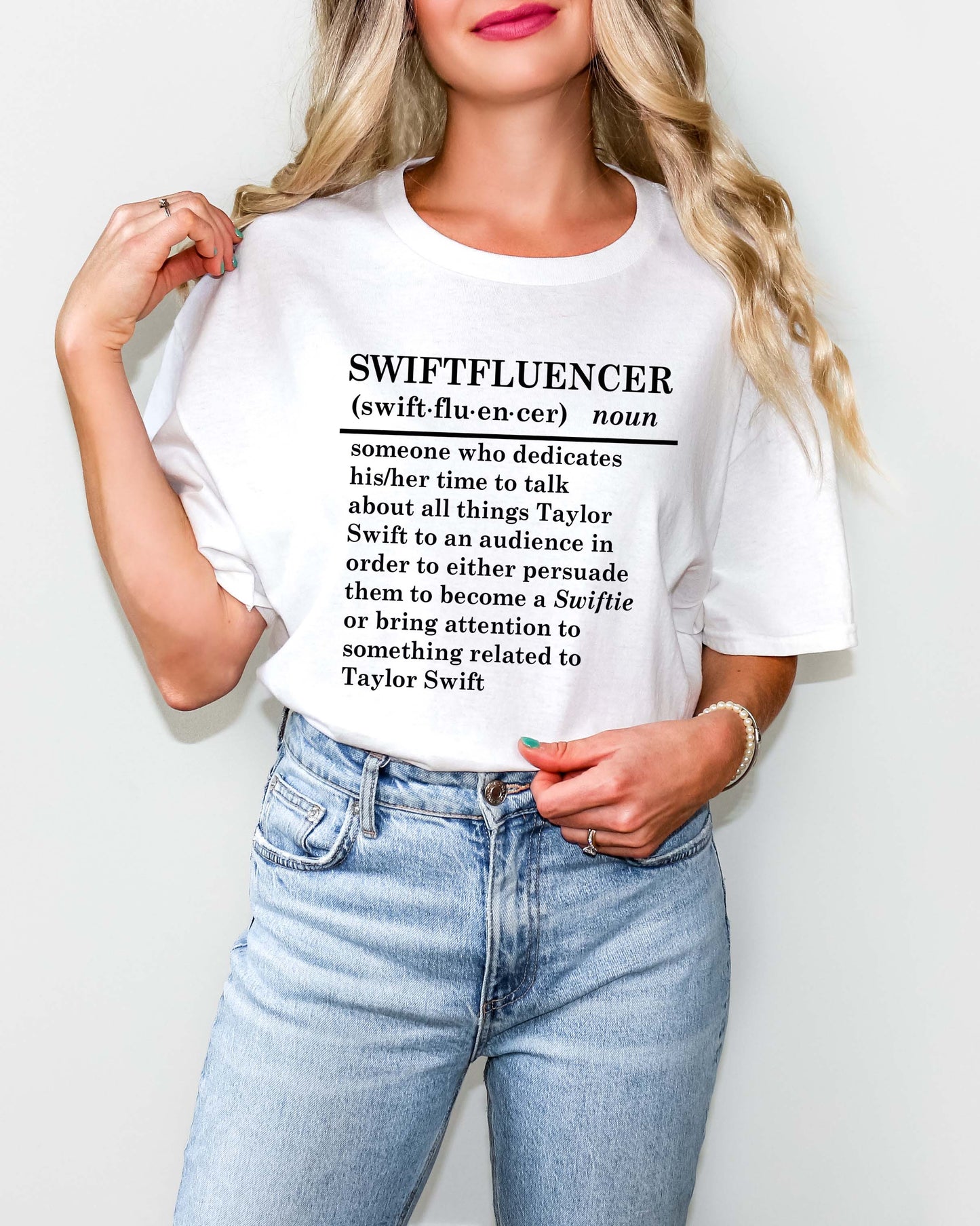 Woman wearing a white t-shirt with the word ‘Swiftfluencer’ and a dictionary-style definition about Taylor Swift fans and content creators. Paired with light wash jeans