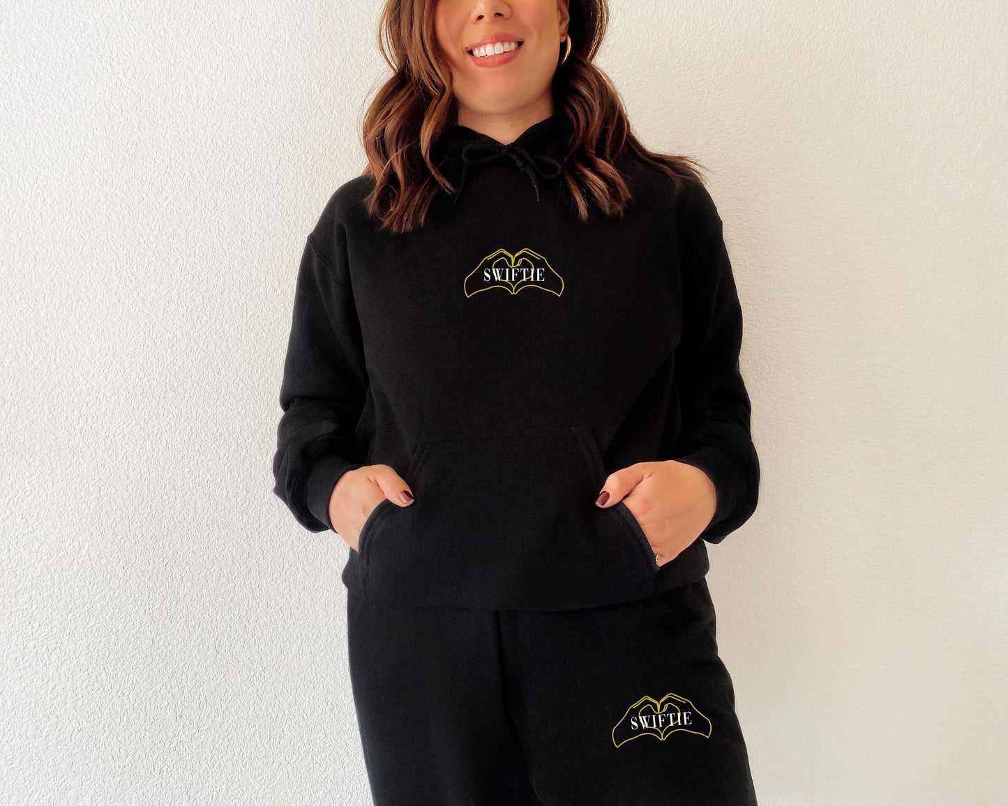 Woman wearing black Swiftie hoodie and joggers set with gold heart hands graphic