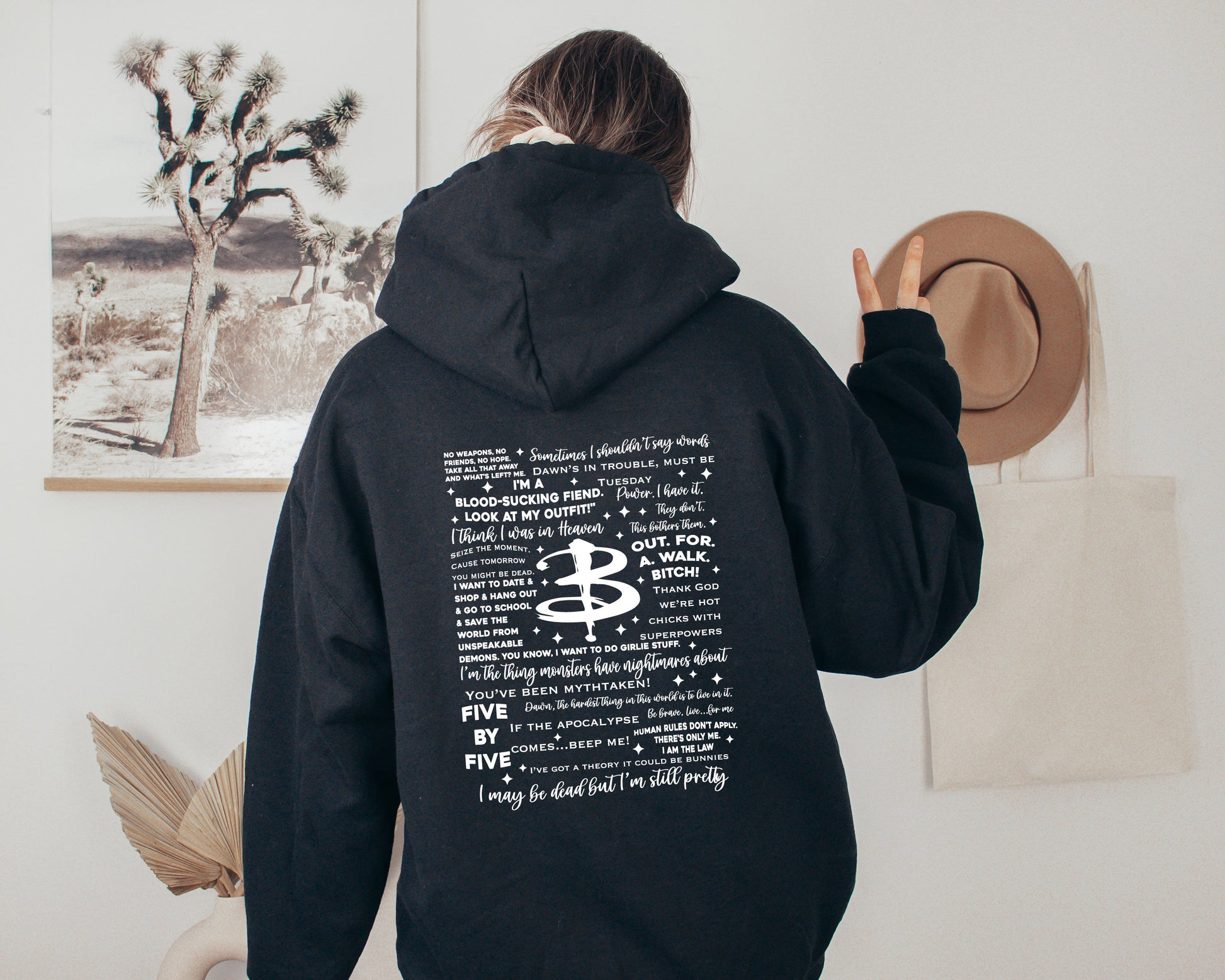 Cozy black fanmade Buffy hoodie with iconic show quotes printed on the back, modeled in a minimalist bedroom setup