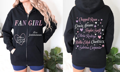 Front view: Woman wearing black hoodie with “Fan Girl” and “It’s a femininenomenon” quotes.

Back view: Artist name print featuring Taylor Swift, Olivia Rodrigo, Sabrina Carpenter, Billie Eilish, and more in pastel hearts and stars.