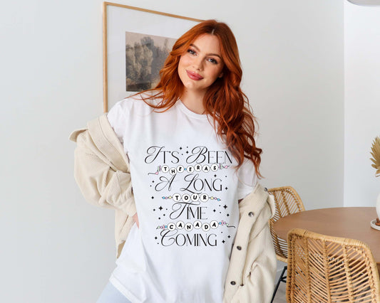 Red-haired woman wearing a white Taylor Swift-inspired t-shirt that reads “It’s Been a Long Time Coming” with The Eras Tour and Canada spelled out in friendship bracelet lettering
