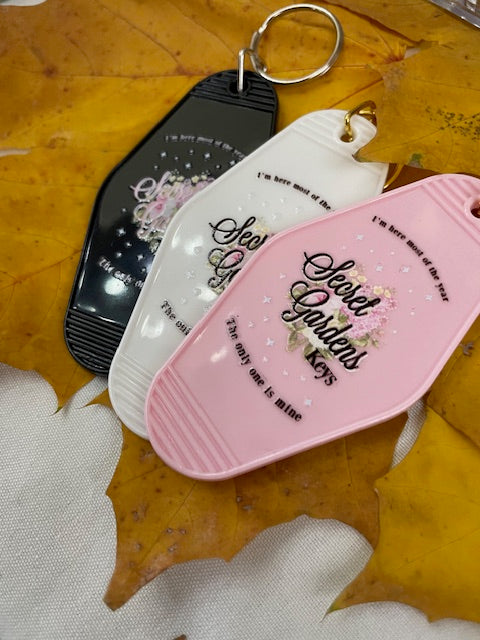 Pink, white, and black Secret Gardens motel keychains inspired by Taylor Swift's I Hate It Here
