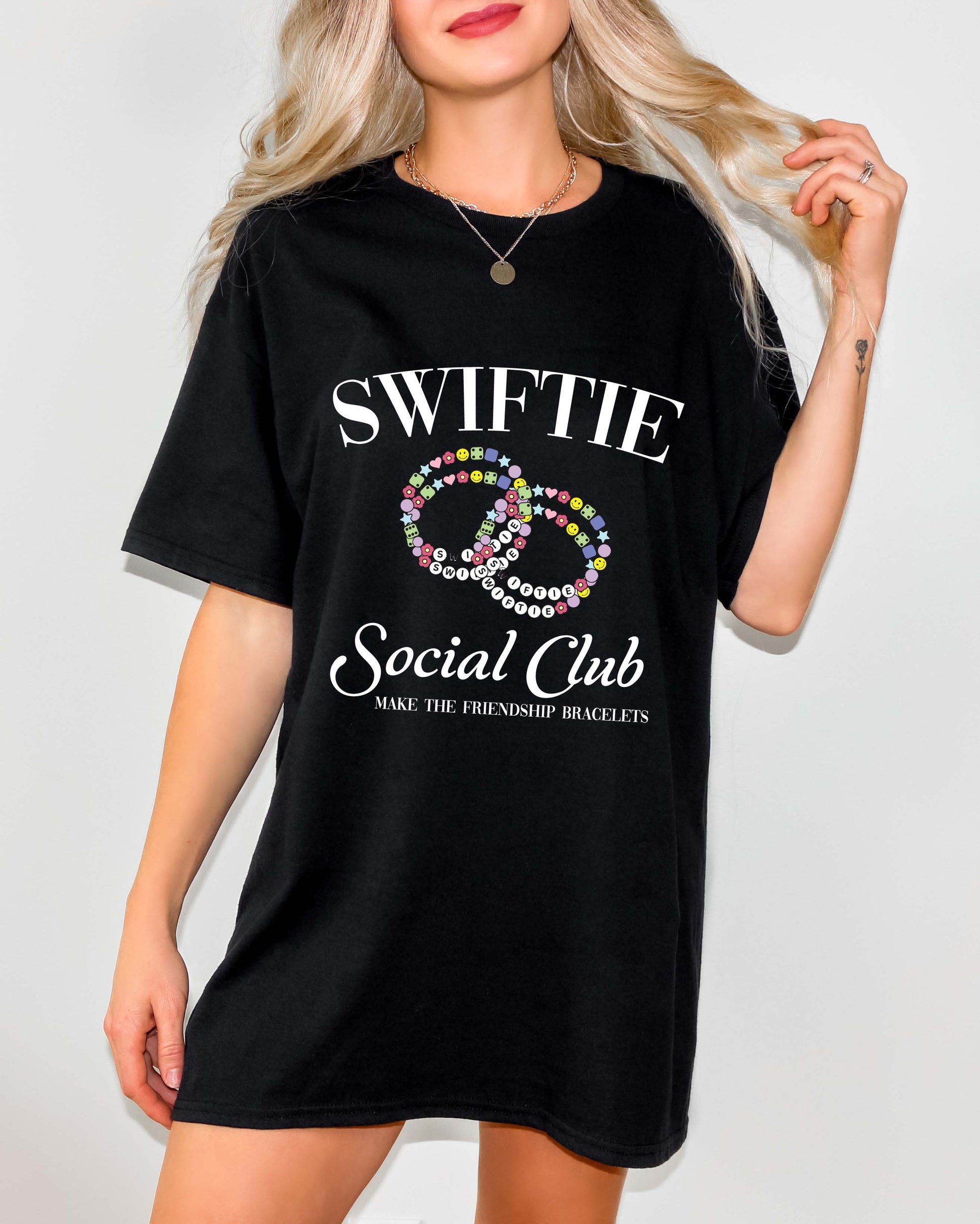 Woman wearing a black oversized t-shirt dress with a colorful friendship bracelet graphic and “Swiftie Social Club” text