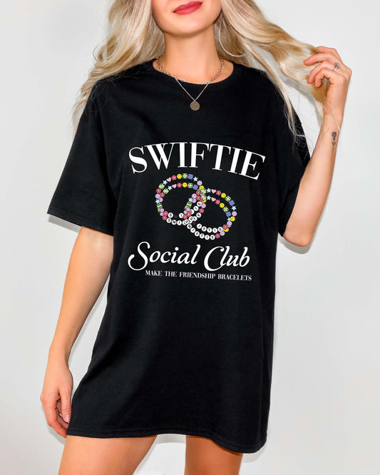 Woman wearing a black oversized t-shirt dress with a colorful friendship bracelet graphic and “Swiftie Social Club” text